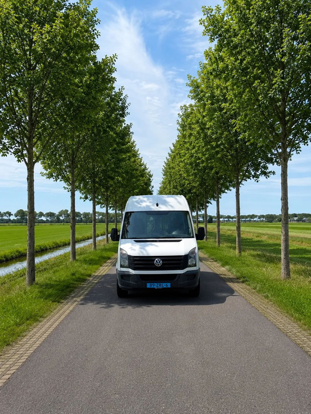 Minibus van Van Asselt op een landweg tussen de bomen in het Groene Hart